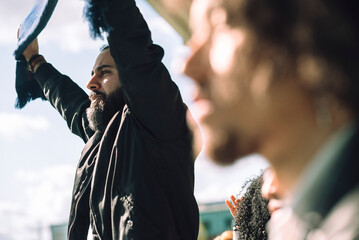 Male fan holding sports scarf cheering from stadium stand at sunny day