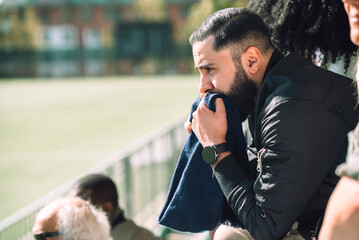 Engaged man sitting with sports scarf while watching game from stadium stand