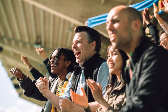Multiracial excited sports fan cheering from stand in stadium at sunny day