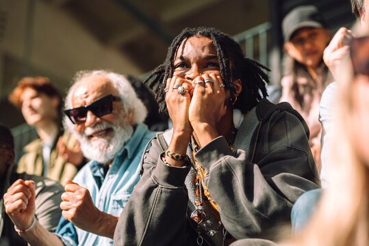 Young male fan biting nails while watching game from sports stadium stand on sunny day