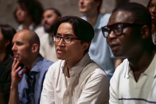 Confused male spectator wearing eyeglasses watching play while sitting at theater