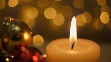 Close-up of a single lit candle illuminating golden Christmas baubles, creating a peaceful and festive holiday mood - Powered by Adobe