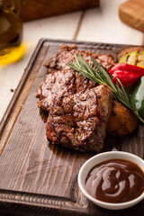 Juicy grilled beef steak portion served on a wooden board with roasted vegetables and herbs