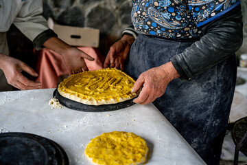 Two elderly women prepare authentic Armenian Gata, shaping dough and nut filling on a floured table, capturing warm homemade culinary tradition.
