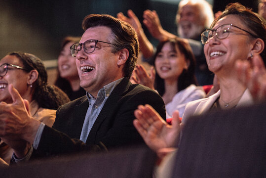 Cheerful mature man clapping with sitting with audience in stage theater