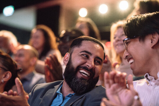 Happy bearded man clapping while enjoying with male friend in stage theater