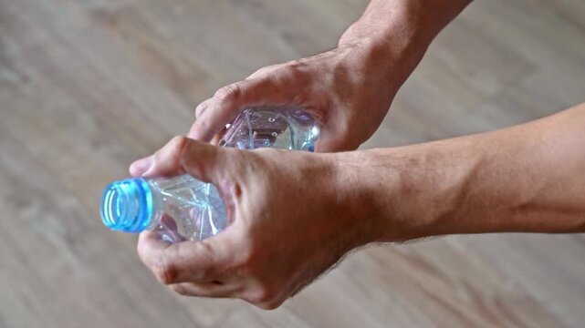 Person crumpling plastic bottle by hand for recycling. Closeup view of bottle crumple and squeeze at home.