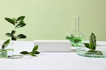 A soft green background with tea leaves and glass beakers filled with tinted liquid suggests both beauty research and herbal experiment aesthetics. Space for product presentation