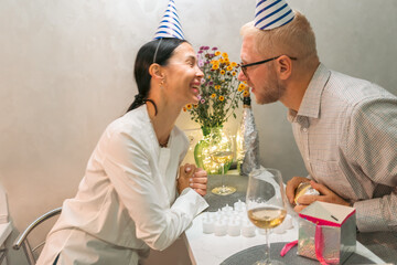 Couple Birthday Celebration Kiss Indoor: Happy couple celebrates birthday with kiss, gifts, and flowers indoors.