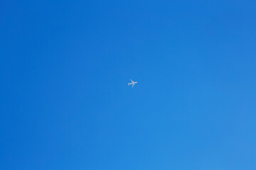 A passenger jet flies high across a bright clear blue sky with no clouds