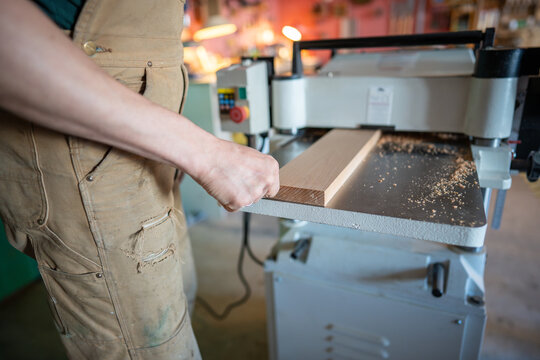 Closeup of carpenter man shaping wooden block on planer thicknesser jointer machine in workshop. Woodworking process, furniture preparation, handmade craftsmanship, precision tools, carpentry studio
