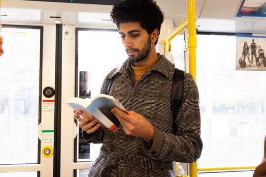 Focused male reader reading booking while traveling in bus
