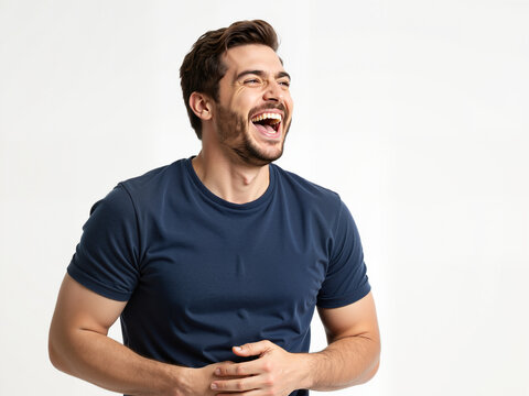 A cheerful man with dark hair is laughing heartily while standing against a plain background, exuding happiness and positivity in a casual blue t-shirt, radiating joy and energy