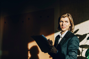 Short haired female business professional holding paper looking away while standing in dark board room at law firm