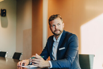 Male law professional looking away while sitting at table in office board room