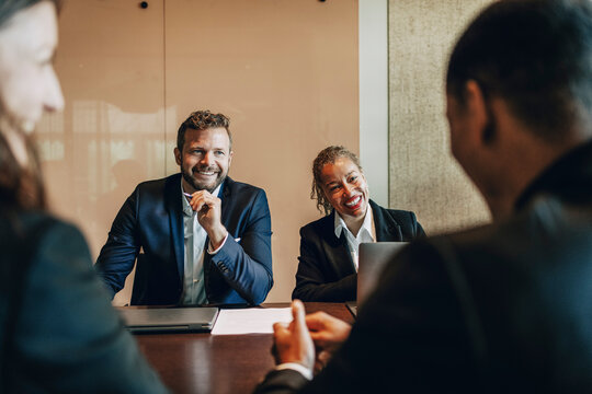 Happy male and female law experts discussing with colleagues while sitting in meeting room at office
