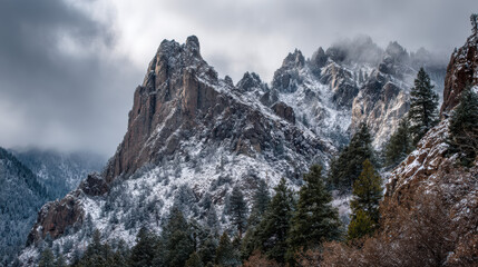A breathtaking view of snow-dusted jagged mountain peaks rising majestically above a forest of evergreen trees under a cloudy and overcast winter sky landscape.