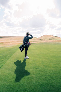 Full length of mature female golfer standing on green golf course against cloudy sky