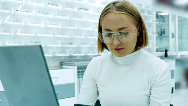 The woman is using a laptop in an optical shop while wearing glasses