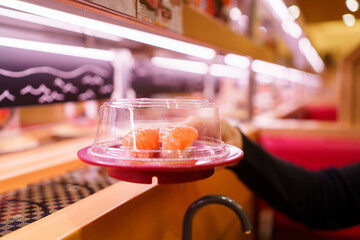 Customer selecting salmon nigiri sushi from conveyor belt restaurant.