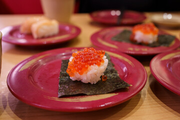 Fresh ikura sushi on a red plate at a Japanese conveyor belt restaurant.