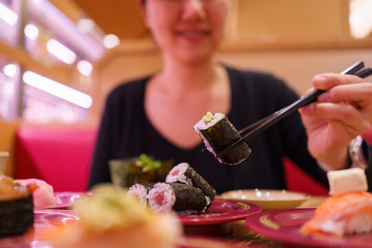 Woman holding Maguro maki sushi with chopsticks in Japanese sushi restaurant.