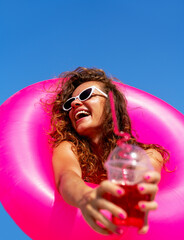 Naklejka premium Woman embracing vacation vibes with drink and pink swim ring.