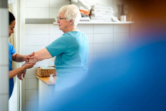 Female caregiver cleaning hands of senior woman in bathroom at home