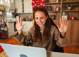 Smiling female in Christmas reindeer antlers having online meeting with family. © Barillo_Images