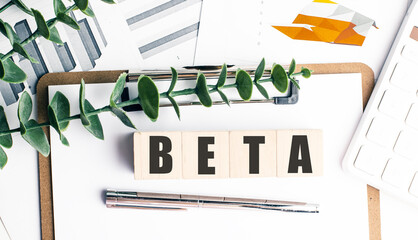 BETA word on wooden blocks with clipboard, charts, pen, calculator, and green leaves on white background