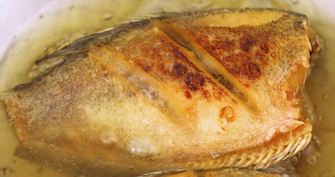 Deep-frying Thai-style snakeskin gourami in hot oil, close-up cooking footage.
