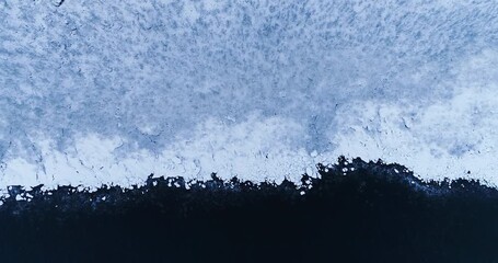 Cinematic top-down aerial drone footage of abstract Arctic coastline on Senja, with cracked sea ice, jagged white shoreline and deep dark blue ocean creating minimalist winter texture - Powered by Adobe