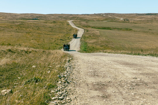 The trucks carry rolls of hay in the winding road in the Caucasus region. After the harvest. Early autumn.