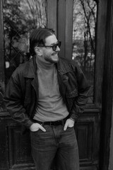Obraz premium Stylish young man wearing glasses posing in front of a modern building, black and white portrait photograph
