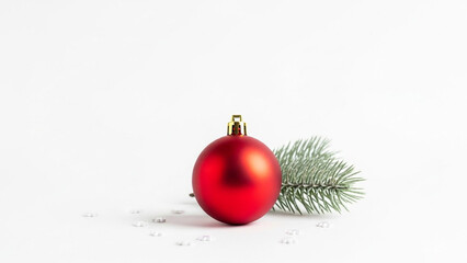 A single, isolated, matte red christmas bauble with a pine tree sprig and scattered snowflake confetti on a clean white background.