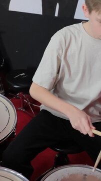 Focused teenage drummer practicing rhythms on drum kit in a modern music studio