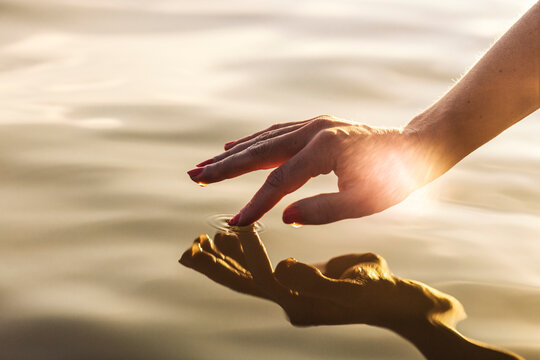 Sunlight shining on hand of woman touching water of lake