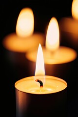 Tea light candles burning, casting warm light in darkness. Close up showing a flame and soft background bokeh. Copy space