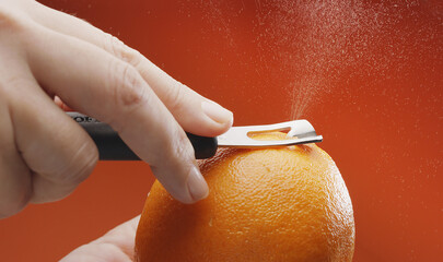 Getting orange peel with a special kitchen tool; orange juice with essential oils sprinkling out...