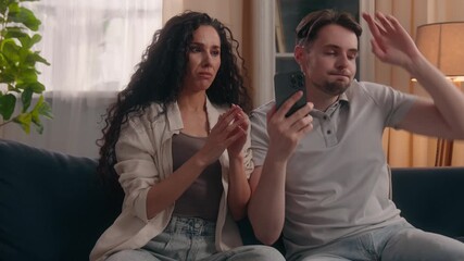 Multiethnic upset couple Caucasian man Hispanic woman crossing fingers hoping result mobile phone at home worried family male female wish win fail checking smartphone online bet losing disappointment - Powered by Adobe