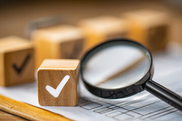 Wooden blocks with white check marks next to a magnifying glass resting on a paper checklist symbolizing detailed inspection and quality control processes