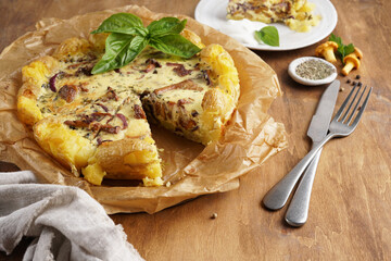 Delicious smash potato quiche pie with chanterelles and cheese cut into pieces and cutlery on wooden table