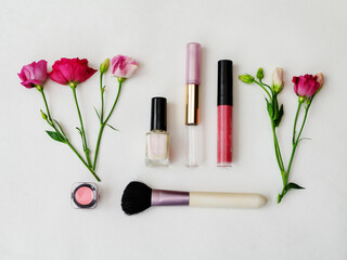 Colorful cosmetics arranged with fresh flowers on a neutral background.