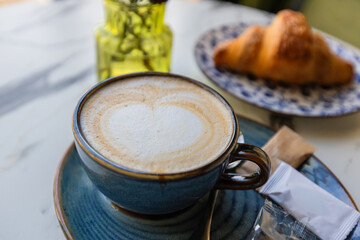 Latte in blue cup with sugar packets and croissant on marble table in cozy café setting