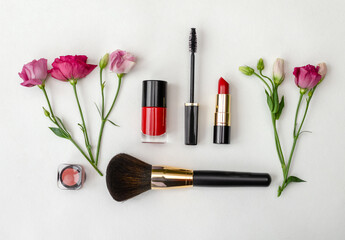 Colorful cosmetics arranged with fresh flowers on a neutral background.