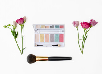 Colorful cosmetics arranged with fresh flowers on a neutral background.