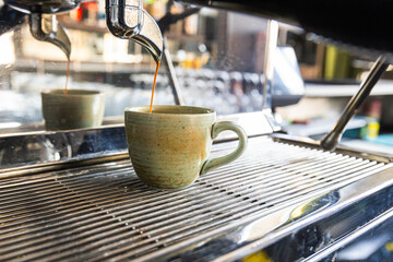 Espresso pouring into ceramic mug from machine in sunlit café with reflections