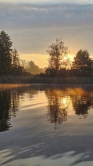 Fototapeta premium A boat ride on a lake at sunrise. Morning light. Tree silhouettes. Fog and reflection.