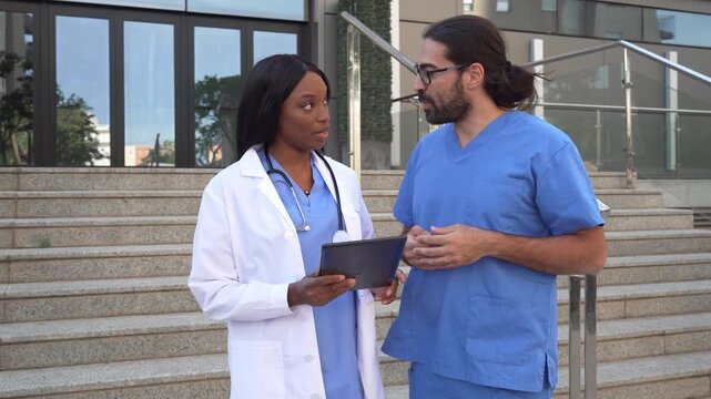 Video of Two diverse healthcare workers reviewing patient data on a tablet outside hospital - Powered by Adobe