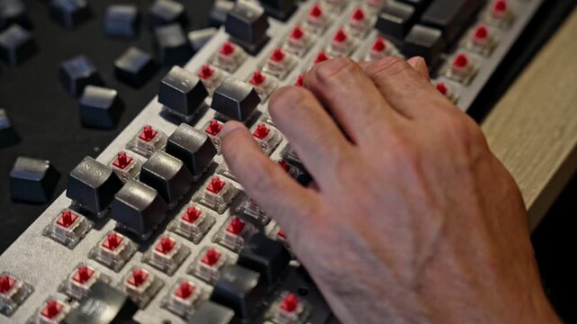 Close up view of man repairing mechanical keyboard, installing keycaps on red switches. Selective focus on hands and keys, concept of electronics, DIY, and computer maintenance